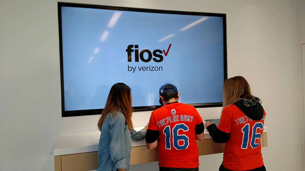 Three participants in front of a screen at a live Verizon event.