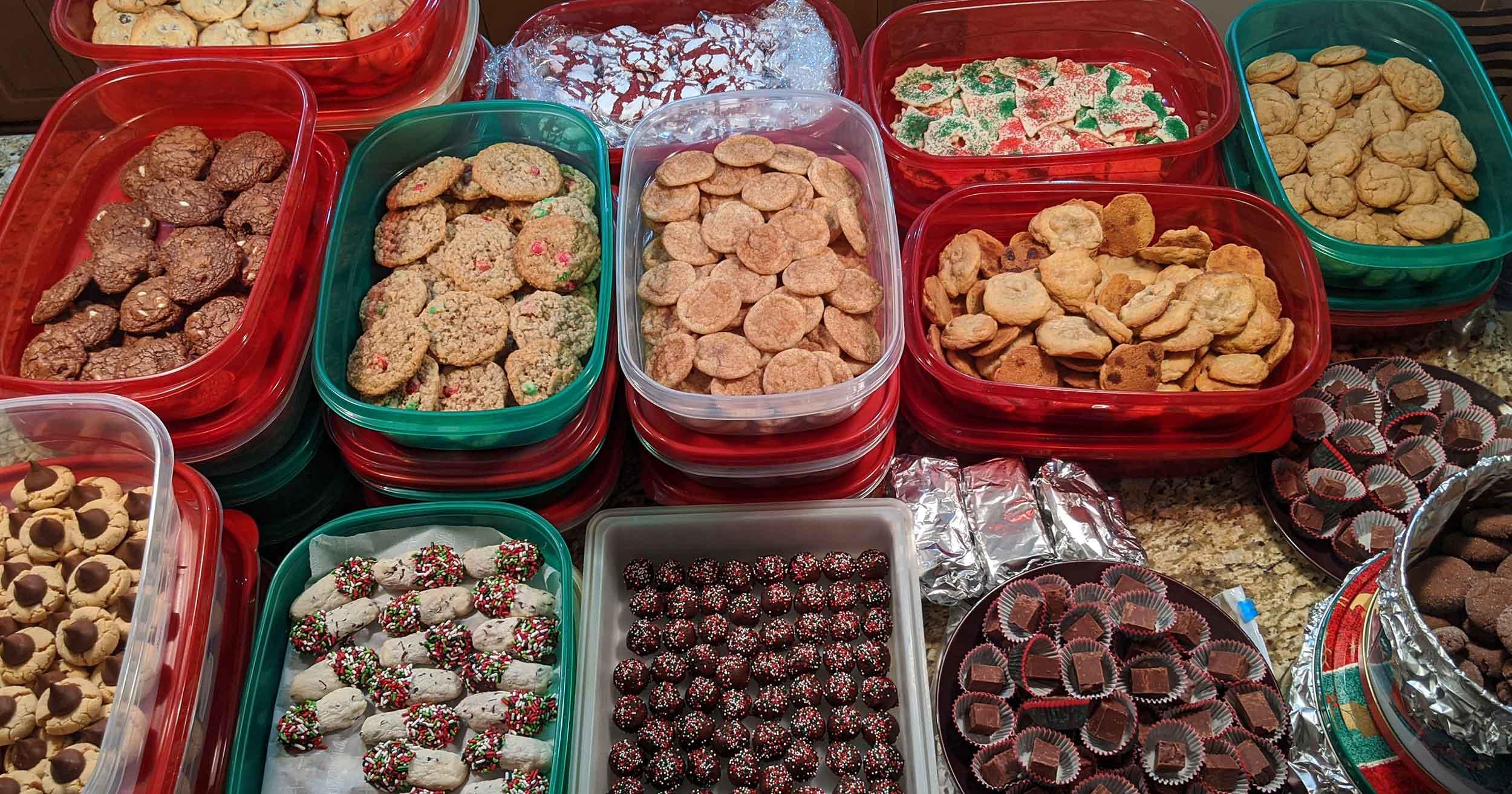 Large kitchen island packed to the edges with stacked tupperware containers full of different types of cookies